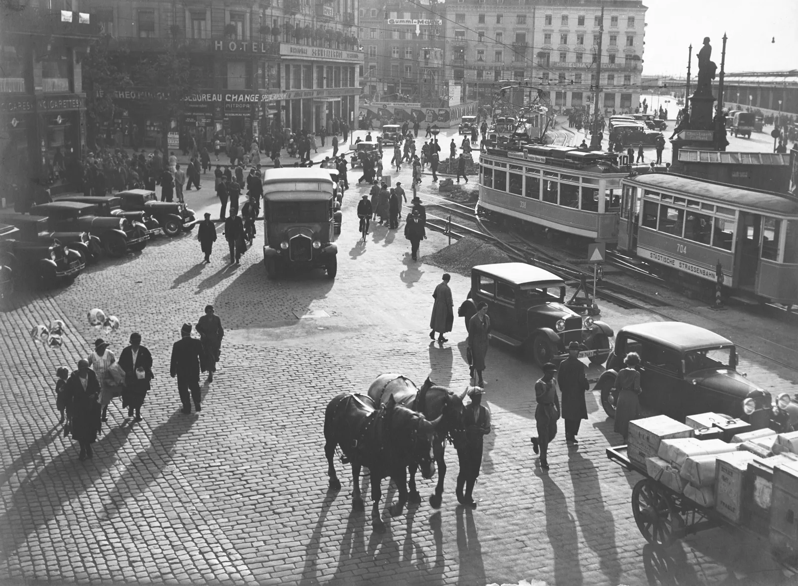 Autos, Pferde und (elektrische) Trams drängen sich auf dem Bahnhofplatz in Zürich, um 1930.