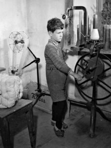 Petit garçon travaillant au rouet à la maison, vers 1940.