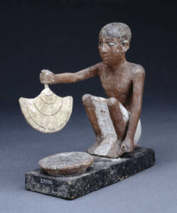 Männlicher Diener, der mit einem Handfächer eine Speise kühlt oder ein Feuer anfacht. Bemaltes Holz, Ägypten, zwischen 2200 und 1800 v. Chr.