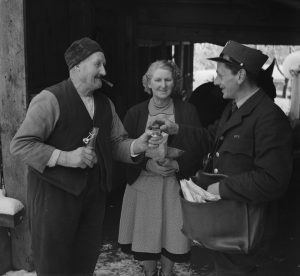 Ein Bauer offeriert dem Pöstler einen Schnaps bei der Postübergabe, 1952.