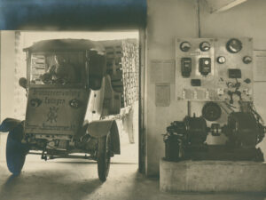 Tribelhorn electric truck belonging to the company Brunnenverwaltung Eptingen, with a charging station on the right, ca. 1920.