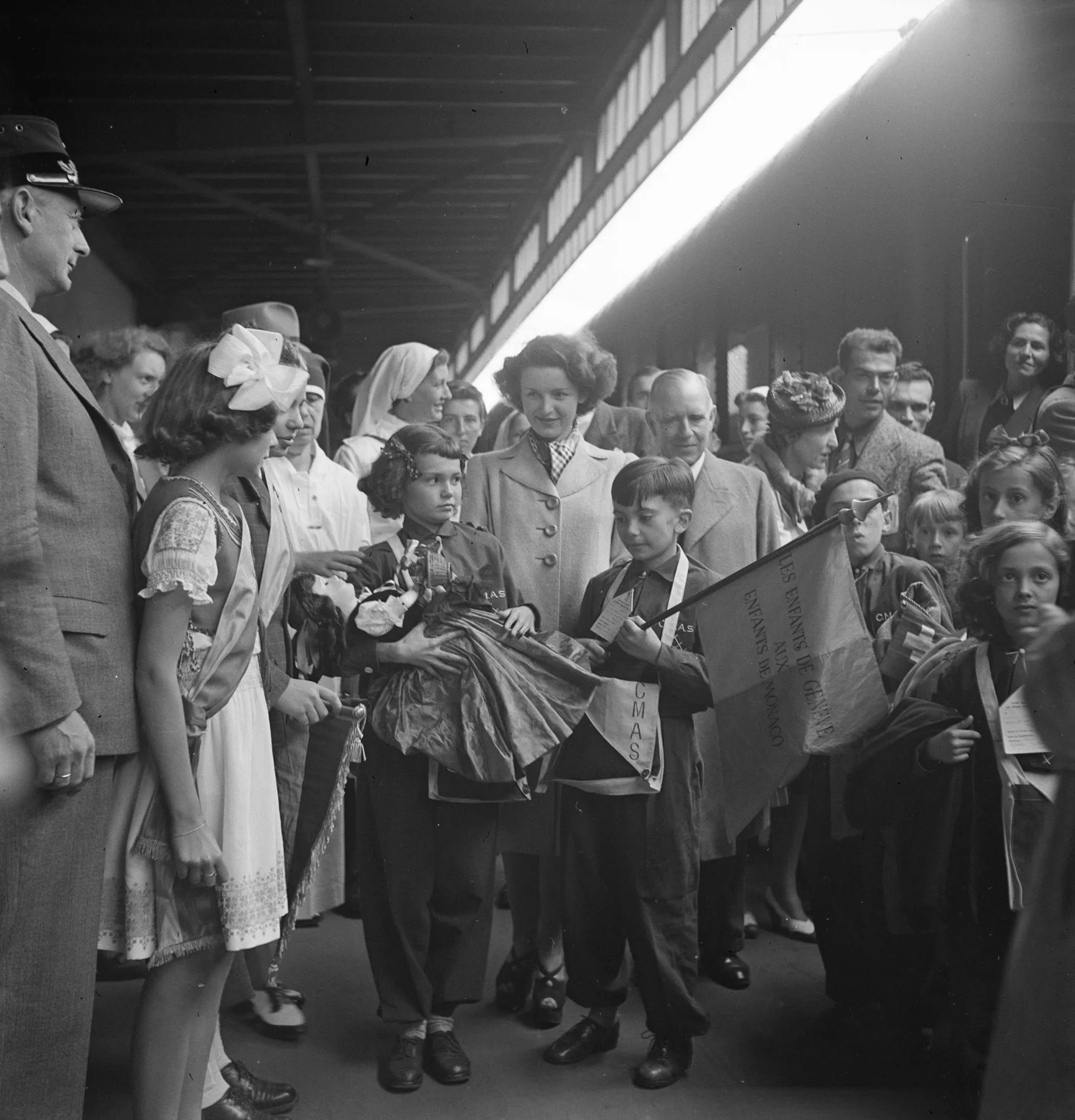 Kinder posieren mit Prinzessin Antoinette von Monaco am Bahnhof Genf, 16. Juni 1942. Der Junge trägt eine Fahne mit der Aufschrift «Les enfants de Genève aux enfants de Monaco».