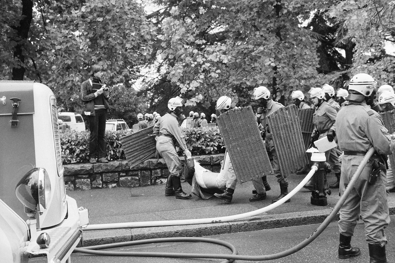 Mehrere Polizisten führen einen jungen Mann an Armen und Beinen knapp über dem Boden ab. Dicht daneben steht ein Fotograf mit seiner Kamera.