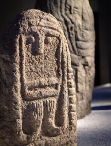 La stèle au premier plan provient du sud de la France et a entre 4400 et 5200 ans. La posture du bras est généralement interprétée comme un geste de vénération ou d’adoration.