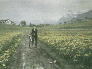 Un homme et sa bicyclette dans une prairie de l’Oberland bernois. En arrière-plan, on aperçoit le Niesen. Vers 1933.