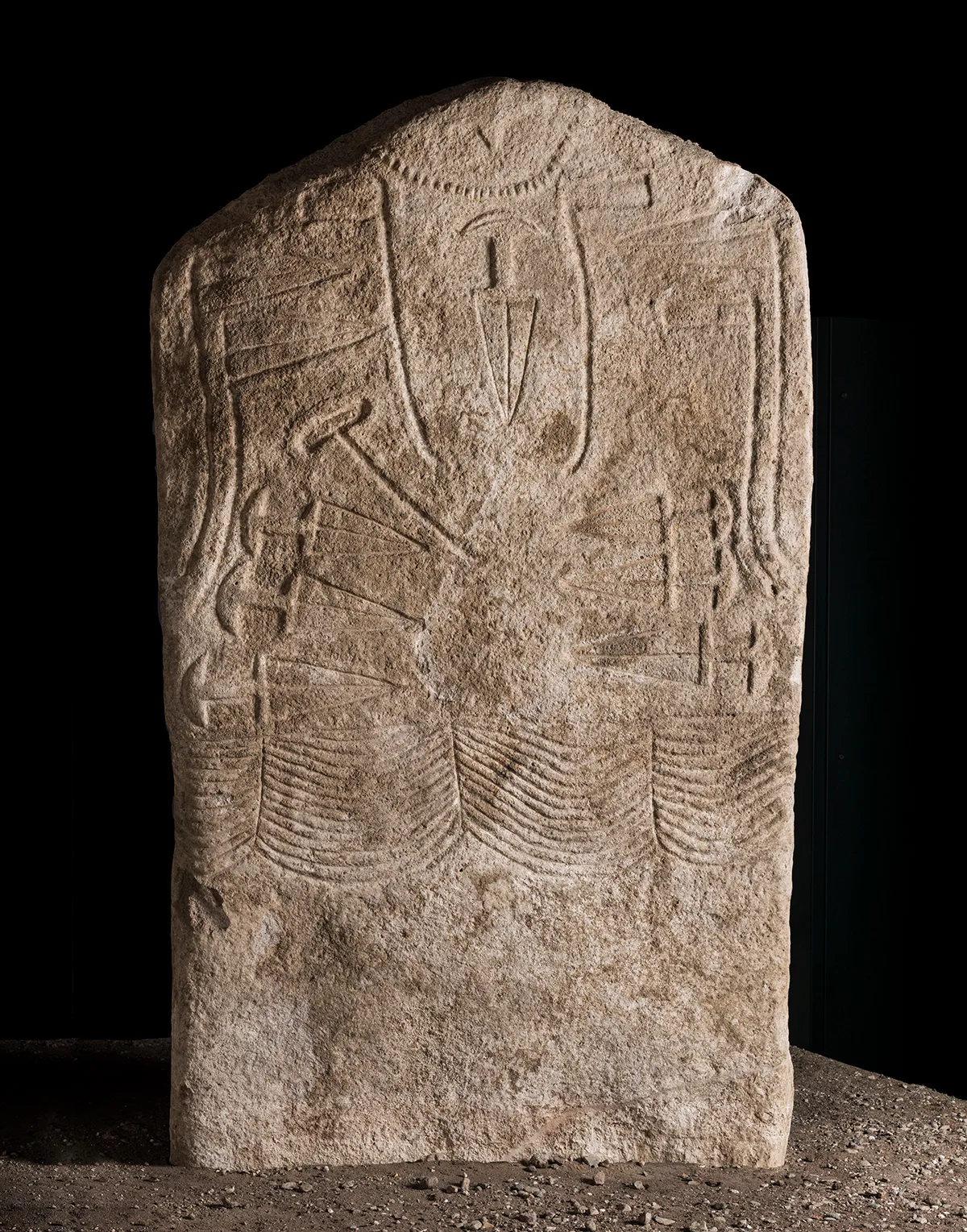 Männliche Stele mit Halskette, Beilen, Dolchen, Streitaxt und mehrreihigem Gürtel. Kalkstein. 3000–2500 v. Chr. Italien, Trentino-Südtirol, Arco.