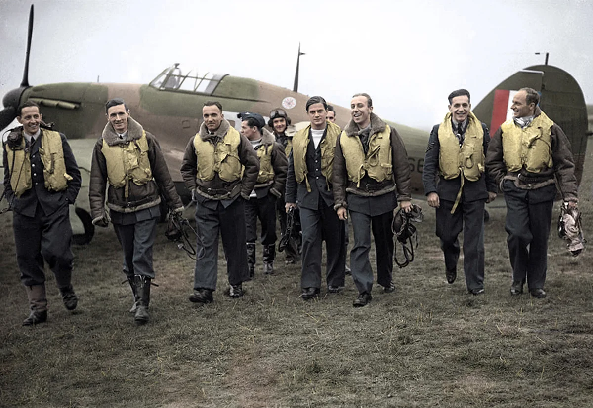 Piloten der 303. Staffel der Royal Air Force. Jan Zumbach steht im Hintergrund und trägt eine Fliegerbrille auf dem Kopf. Koloriertes Foto, um 1940.