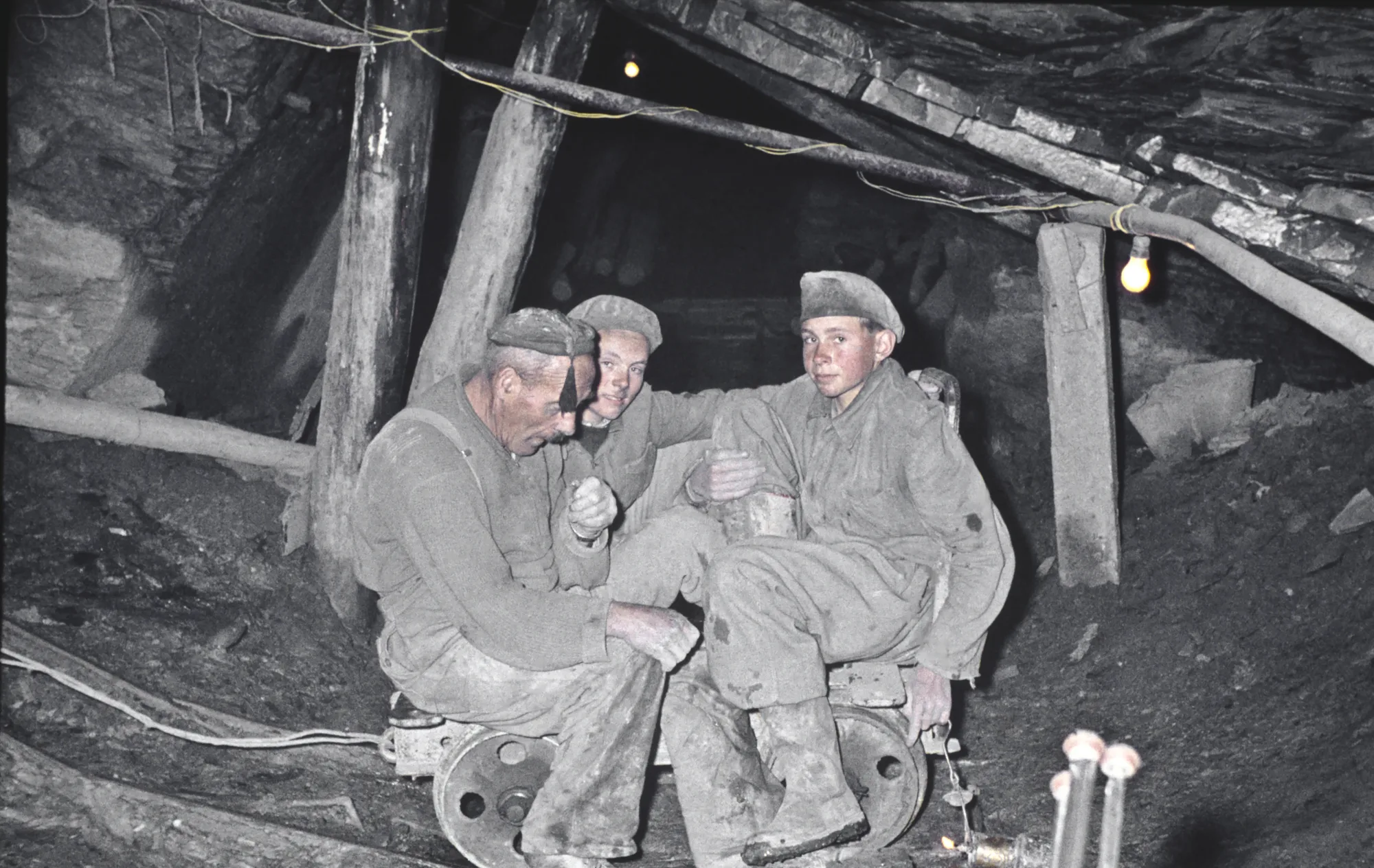 Der Arbeiter Alois Jeremias und zwei seiner Söhne sitzen auf einem Rollwagen in einem Schieferstollen, um 1960.