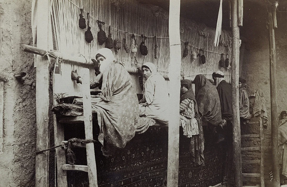 Teppichknüpferinnen in Sultanabad. Die Webstühle befanden sich in der Regel in Privathäuser. Das Teppichknüpfen war Handarbeit und wurde von Frauen verrichtet. Die Teppiche wurden dazu in Webstühlen eingespannt. Das Bild entstand in den 1880er-Jahren.