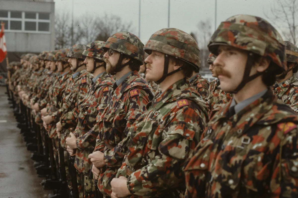 Schweizer Soldaten im Tarnanzug mit Helmüberzug im charakteristischen Muster der Alpenflage, 1979.
