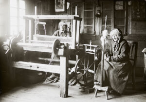 Zwei Frauen in der Stube an der Arbeit: die eine am Spinnrad, die andere am Webstuhl, um 1890.